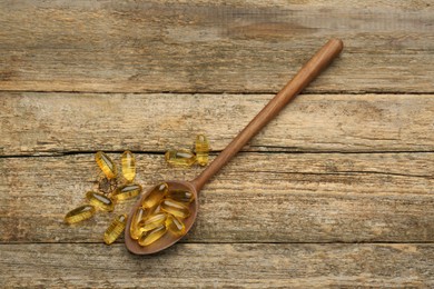 Photo of Vitamin capsules in spoon on wooden table, top view