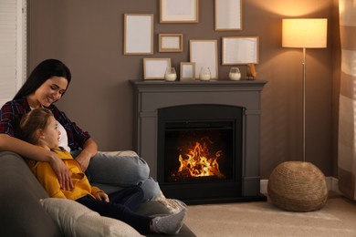 Happy mother and daughter spending time together on sofa near fireplace at home. Space for text