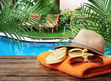 Image of Beach towel, flip flops, hat and sunglasses on wooden surface near outdoor swimming pool
