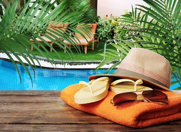 Beach towel, flip flops, hat and sunglasses on wooden surface near outdoor swimming pool