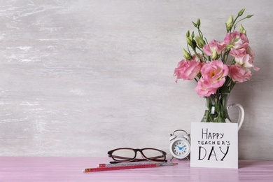 Photo of Card with inscription HAPPY TEACHER'S DAY and vase of flowers on pink table against light wall, space for text