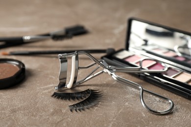 Photo of False eyelashes, curler and makeup products on grey table, closeup