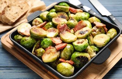 Photo of Delicious Brussels sprouts with bacon in baking pan on blue wooden table