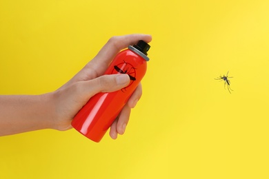 Woman spraying insect repellent on mosquito against yellow background, closeup