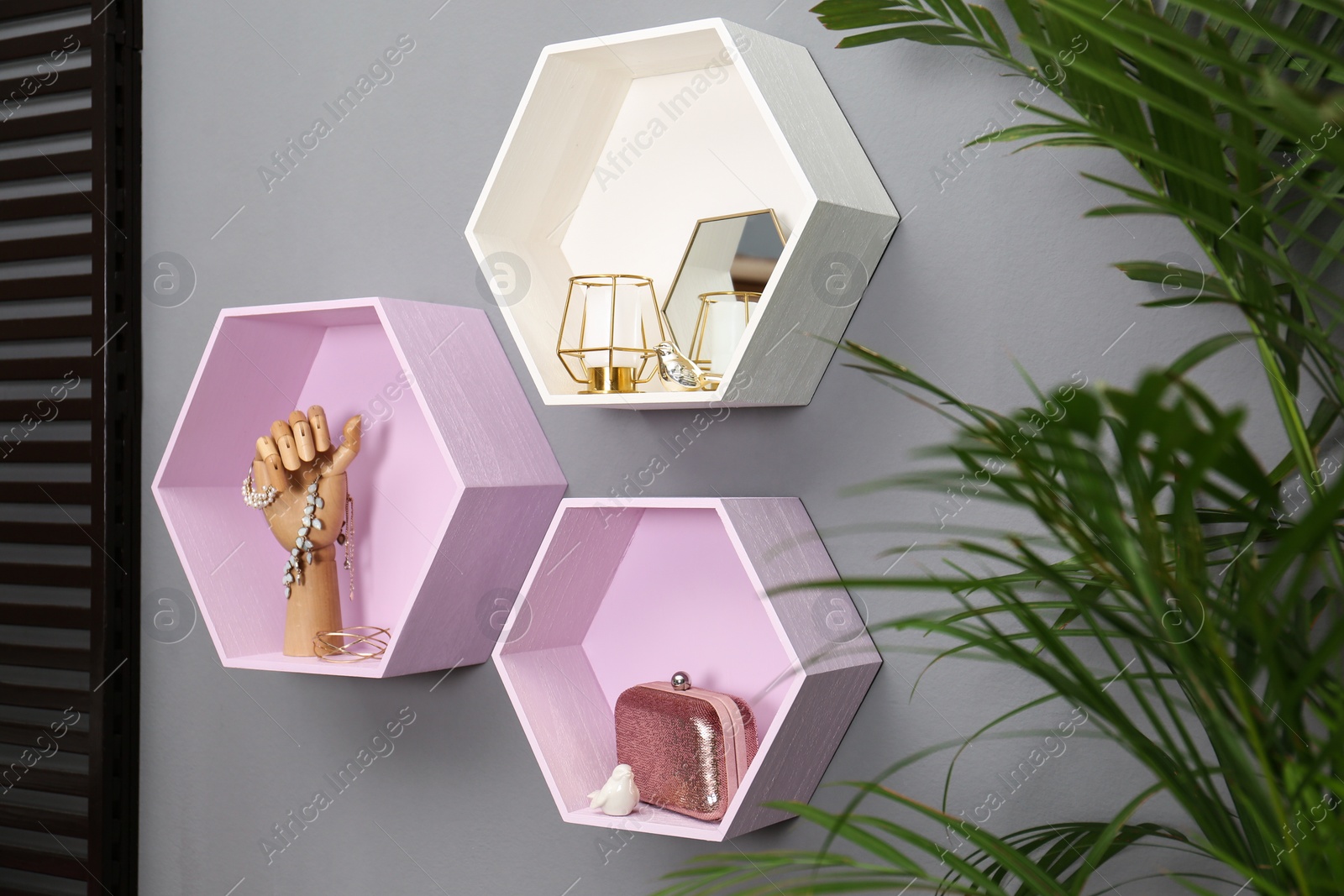 Photo of Hexagon shaped shelves with different stuff on grey wall. Interior design