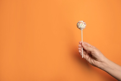 Photo of Woman holding bright delicious cake pop on color background, closeup. Space for text