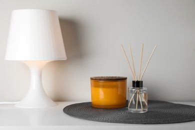 Aromatic reed air freshener, candle and lamp on white table