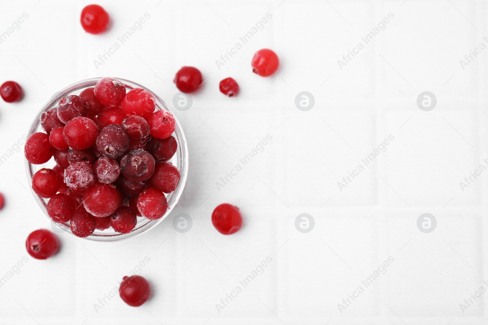 Photo of Frozen red cranberries in bowl on white tiled table, flat lay. Space for text