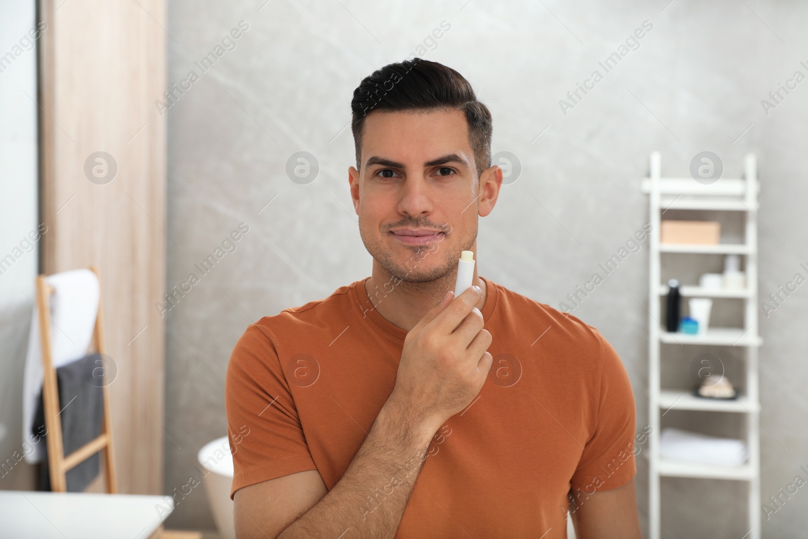 Photo of Man applying hygienic lip balm in bathroom