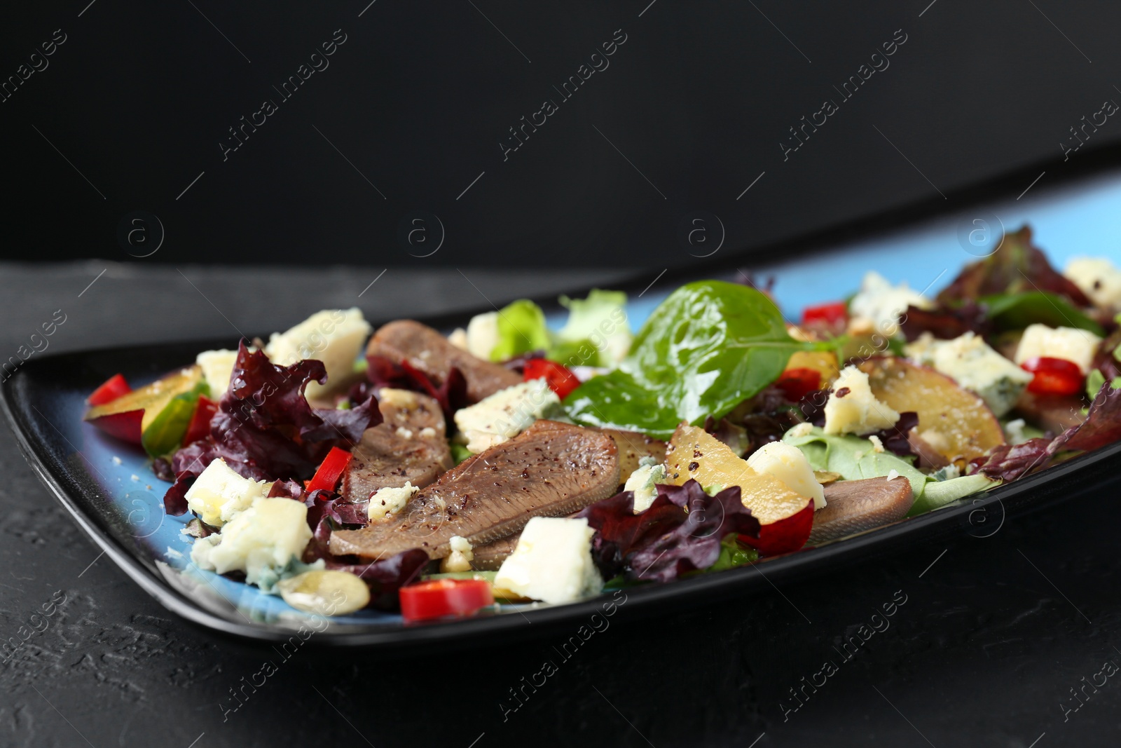 Photo of Delicious salad with beef tongue and cheese on black table, closeup