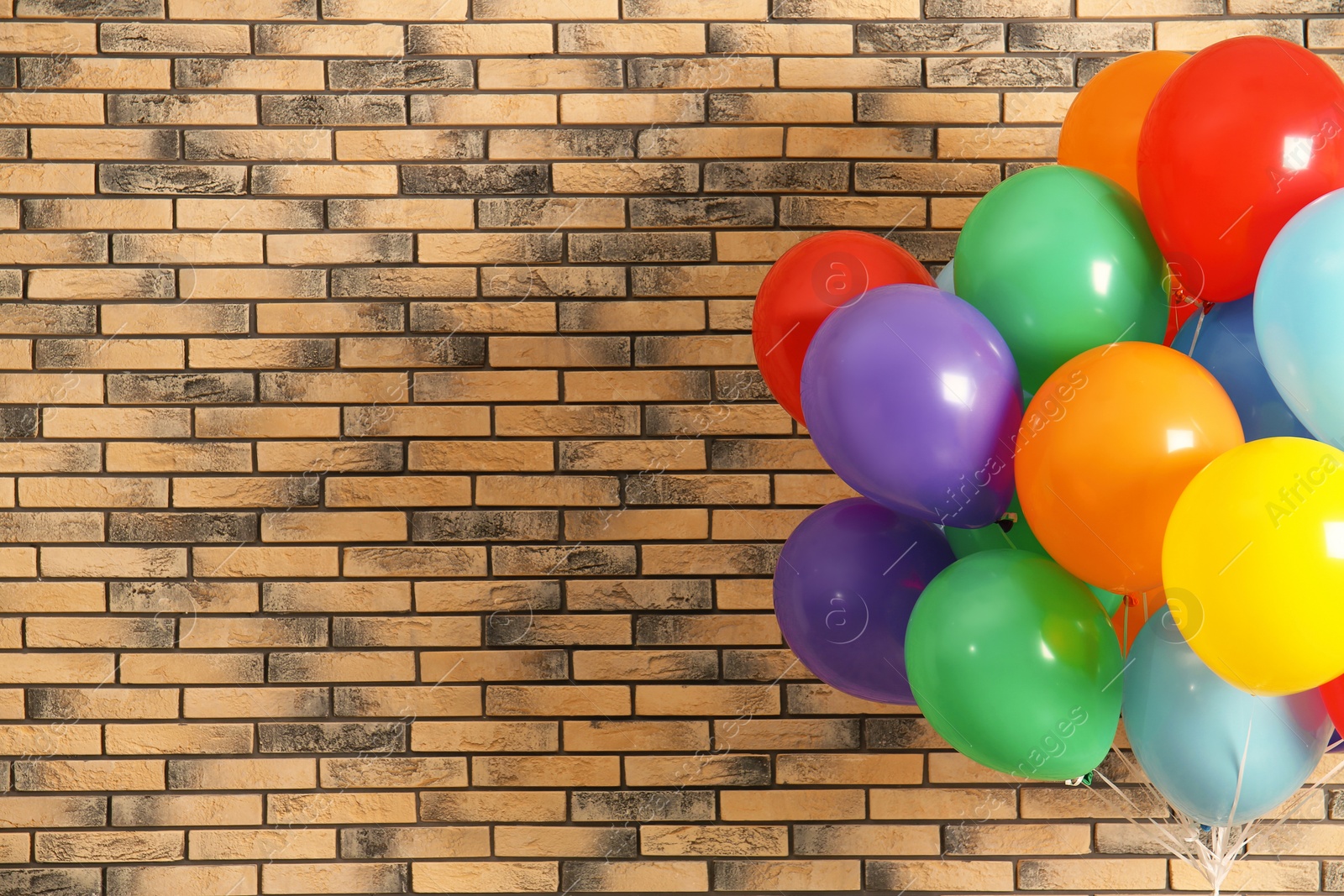 Photo of Bunch of bright balloons and space for text against brick wall