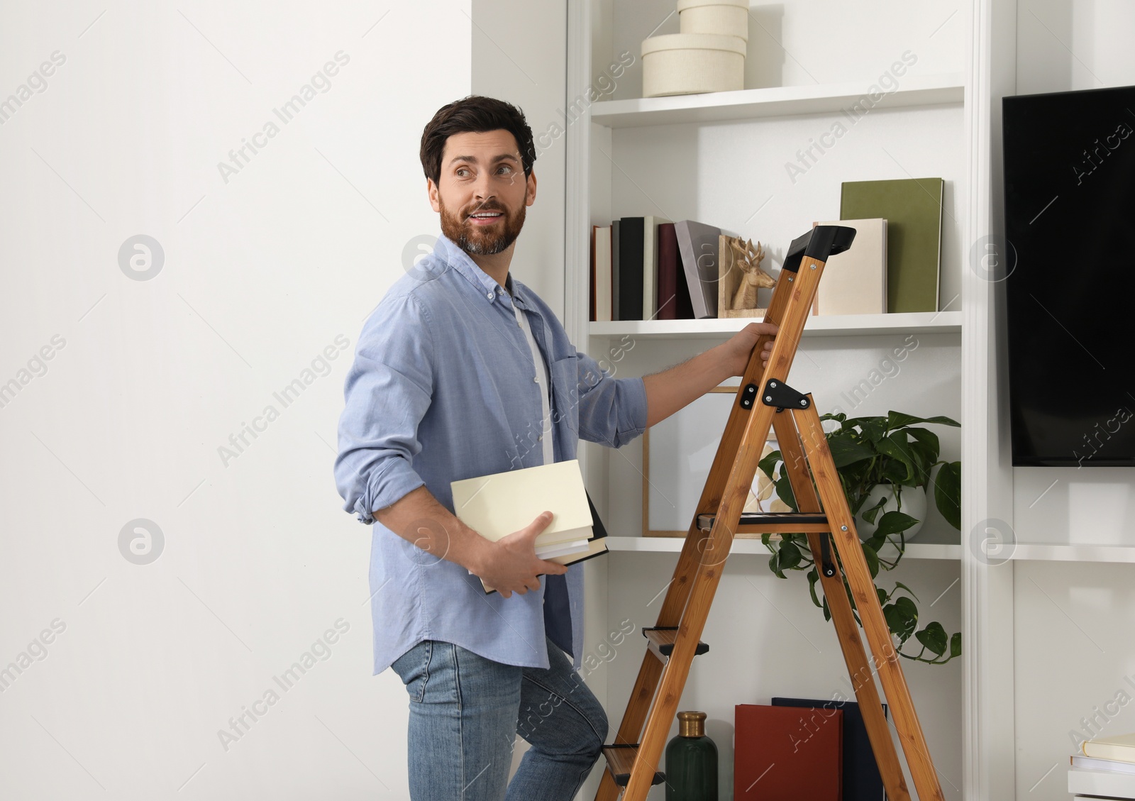 Photo of Man with books on wooden folding ladder at home. Space for text