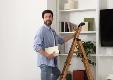 Man with books on wooden folding ladder at home. Space for text