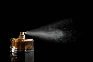 Photo of Spraying bottle of perfume on black background