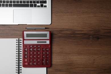 Calculator, office stationery and laptop on wooden table, flat lay. Space for text