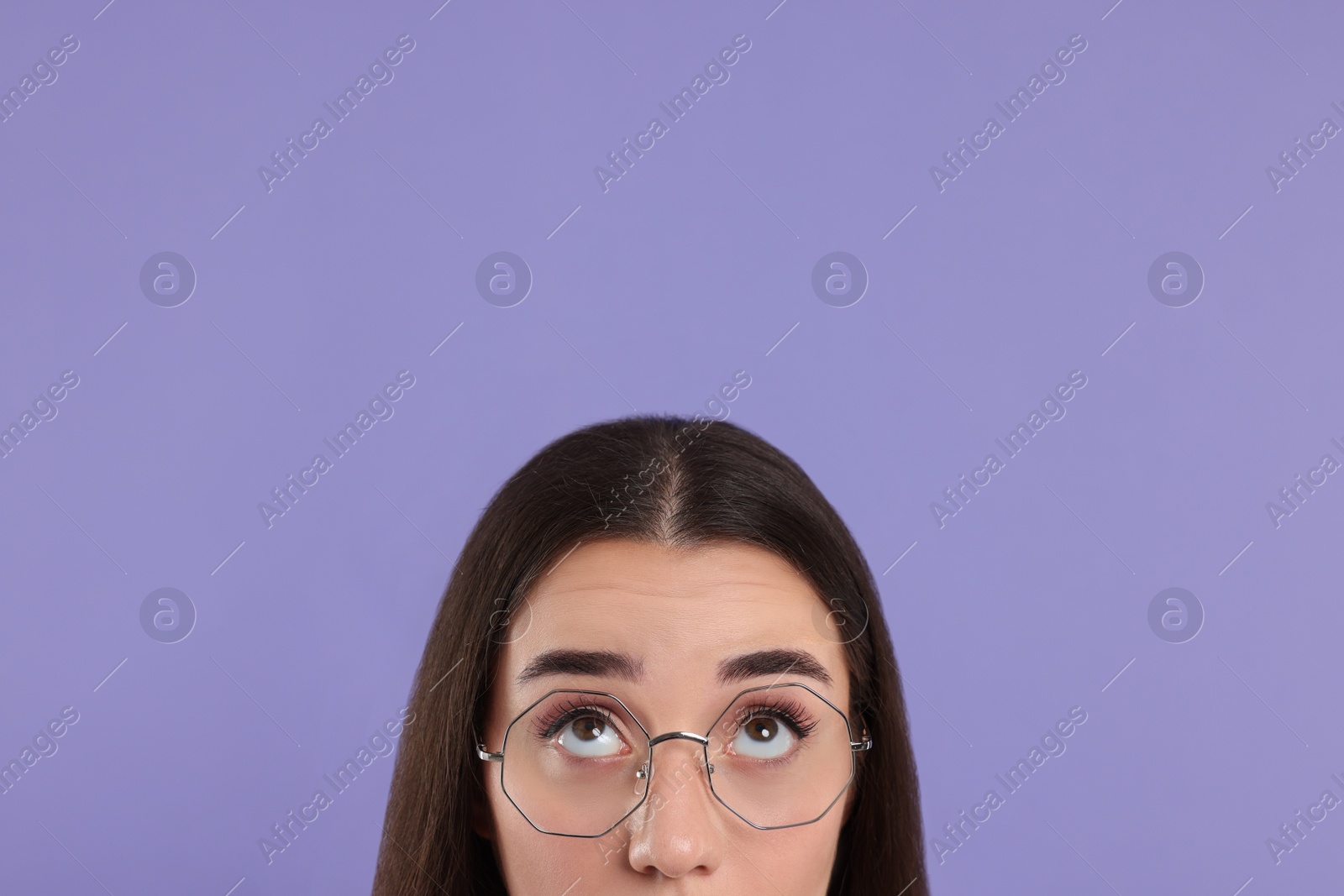 Photo of Woman in glasses looking up on violet background, closeup