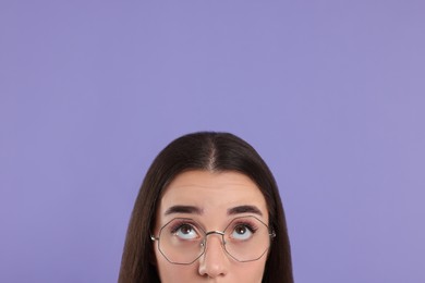 Woman in glasses looking up on violet background, closeup