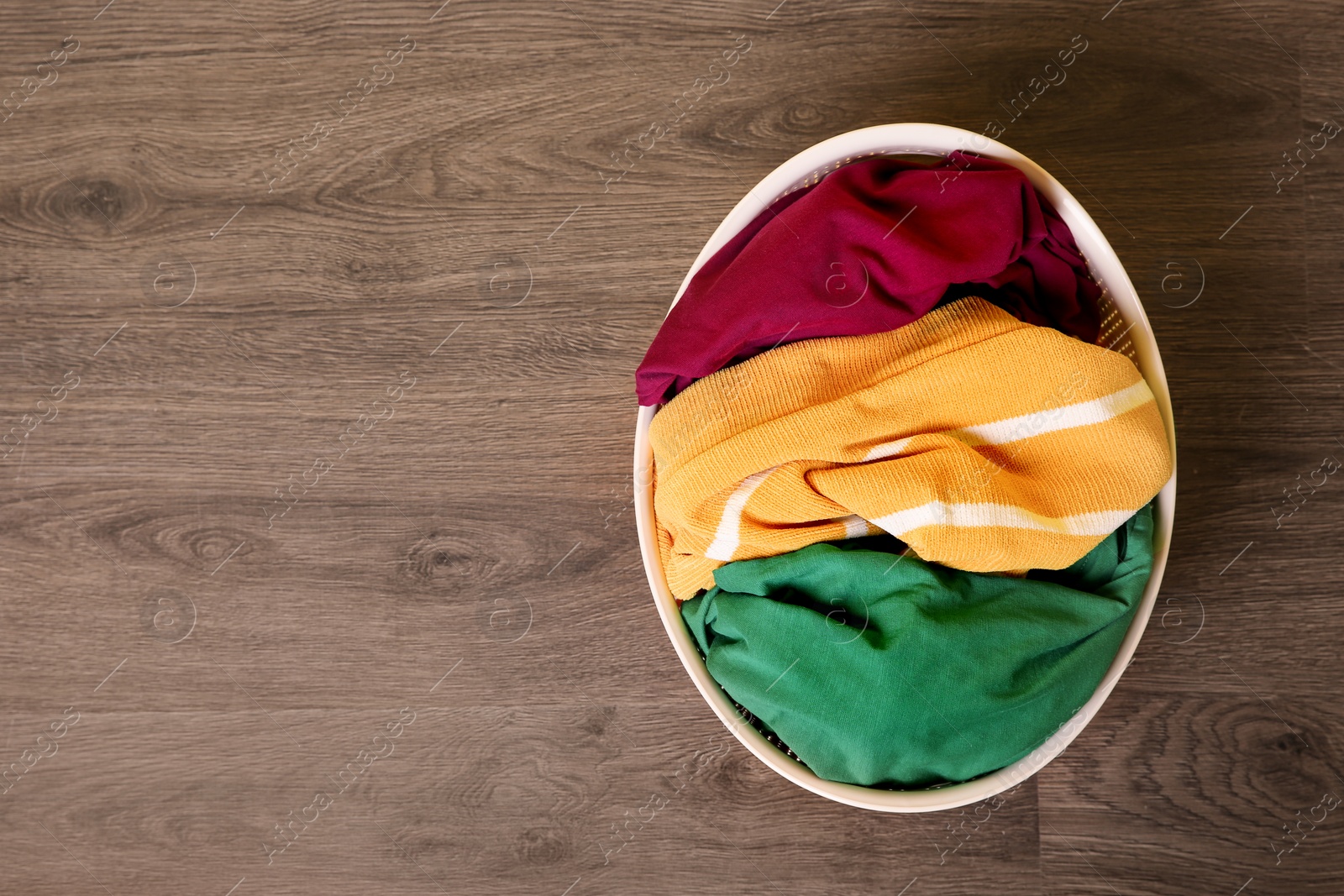 Photo of Laundry basket with dirty clothes on wooden background, top view. Space for text