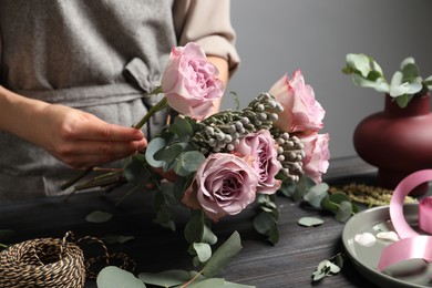 Photo of Florist creating beautiful bouquet at black wooden table indoors, closeup