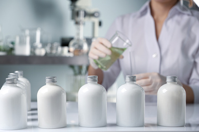 Photo of Scientist working in laboratory, focus on bottles with cosmetic product