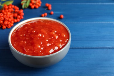 Photo of Delicious rowan jam in ceramic bowl on blue wooden  table. Space for text