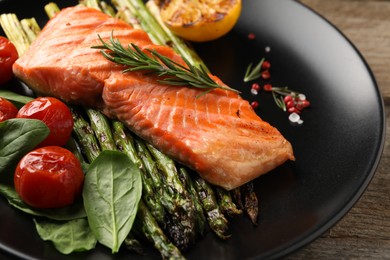 Photo of Tasty grilled salmon with tomatoes, asparagus and rosemary on table, closeup