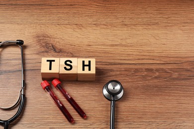 Photo of Endocrinology. Stethoscope, cubes with thyroid hormones and blood samples in test tubes on wooden table. Space for text