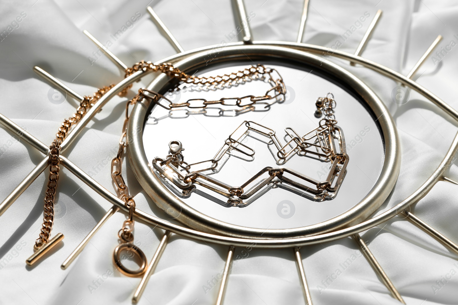 Photo of Metal chains and mirror on white fabric. Luxury jewelry