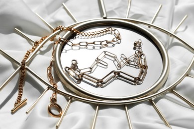 Photo of Metal chains and mirror on white fabric. Luxury jewelry