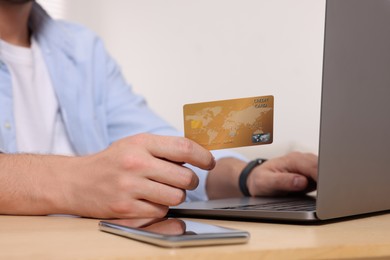 Photo of Man with credit card using laptop for online shopping at wooden table indoors, closeup