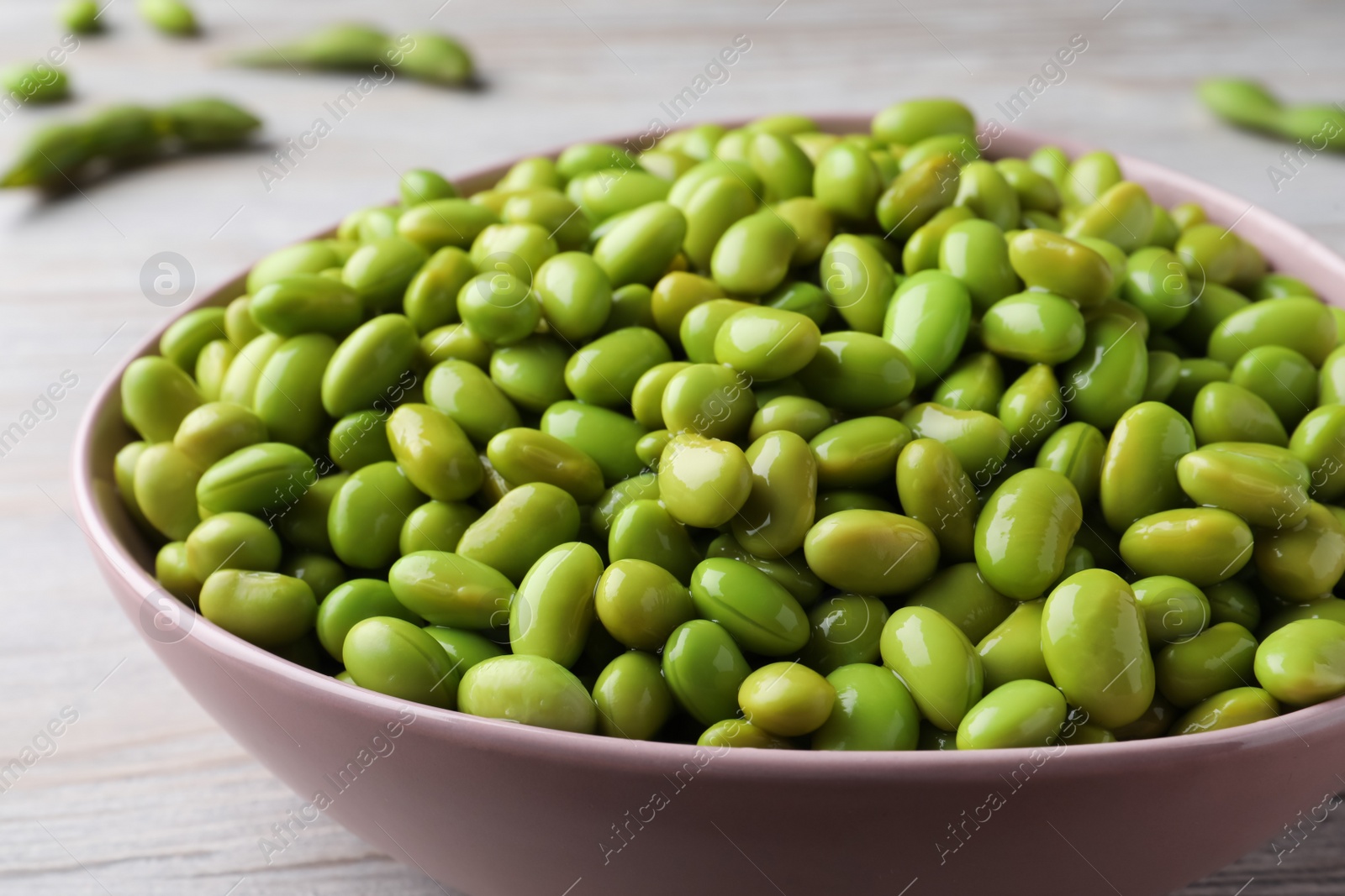 Photo of Bowl of delicious edamame beans on light wooden table, closeup