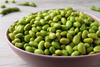 Bowl of delicious edamame beans on light wooden table, closeup