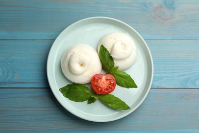 Photo of Delicious burrata cheese with basil and cut tomato on light blue wooden table, top view