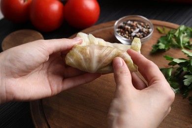 Photo of Woman preparing stuffed cabbage roll at table, closeup