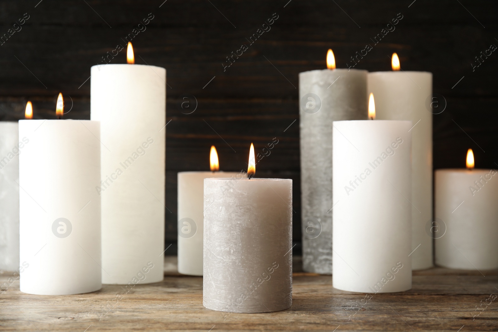 Photo of Many alight wax candles on table against dark background