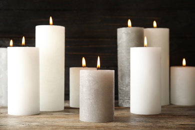 Many alight wax candles on table against dark background