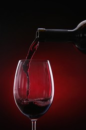 Photo of Pouring red wine from bottle into glass on color background, closeup