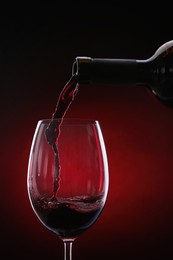 Pouring red wine from bottle into glass on color background, closeup