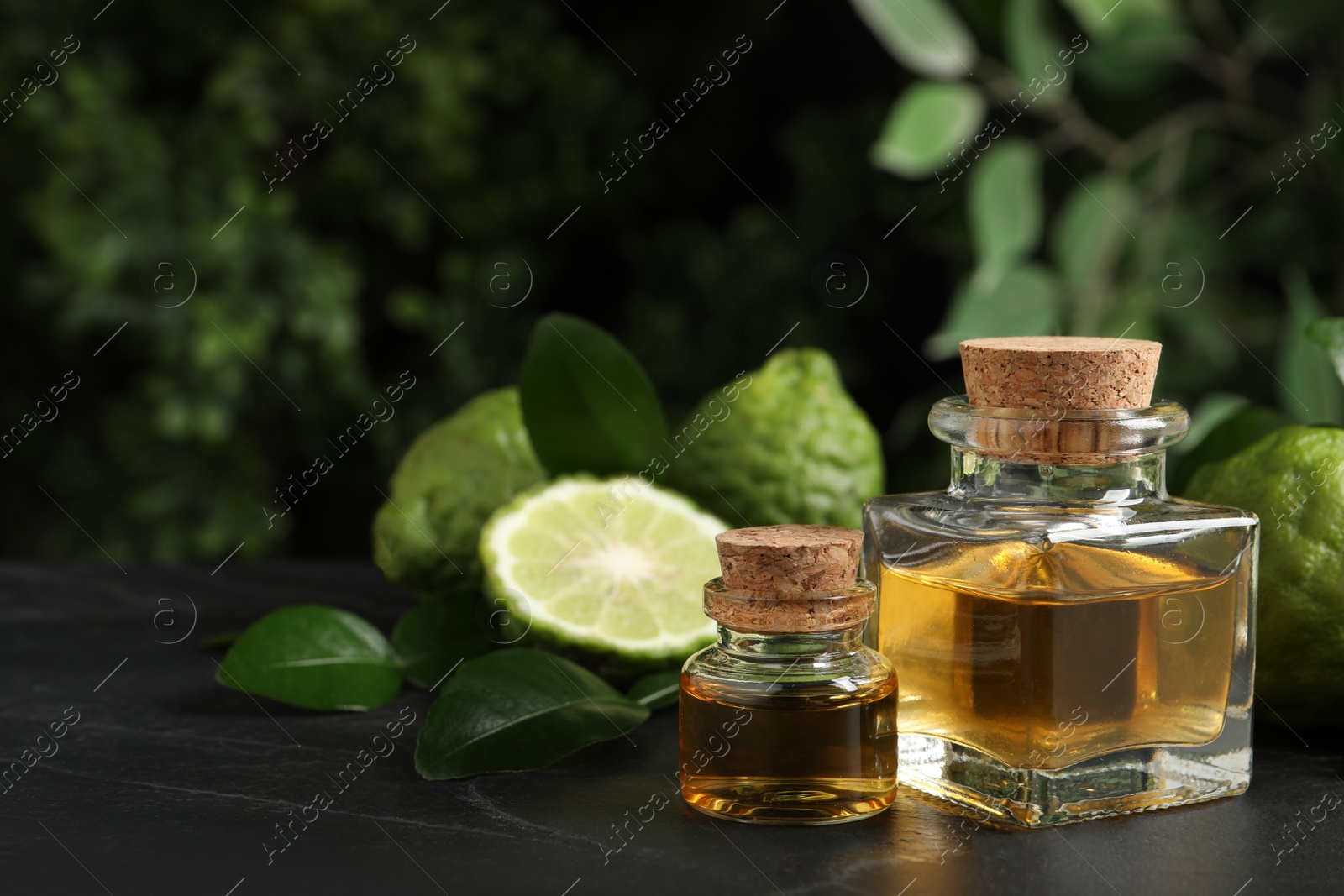 Photo of Glass bottles of bergamot essential oil and fresh fruits on black stone table. Space for text