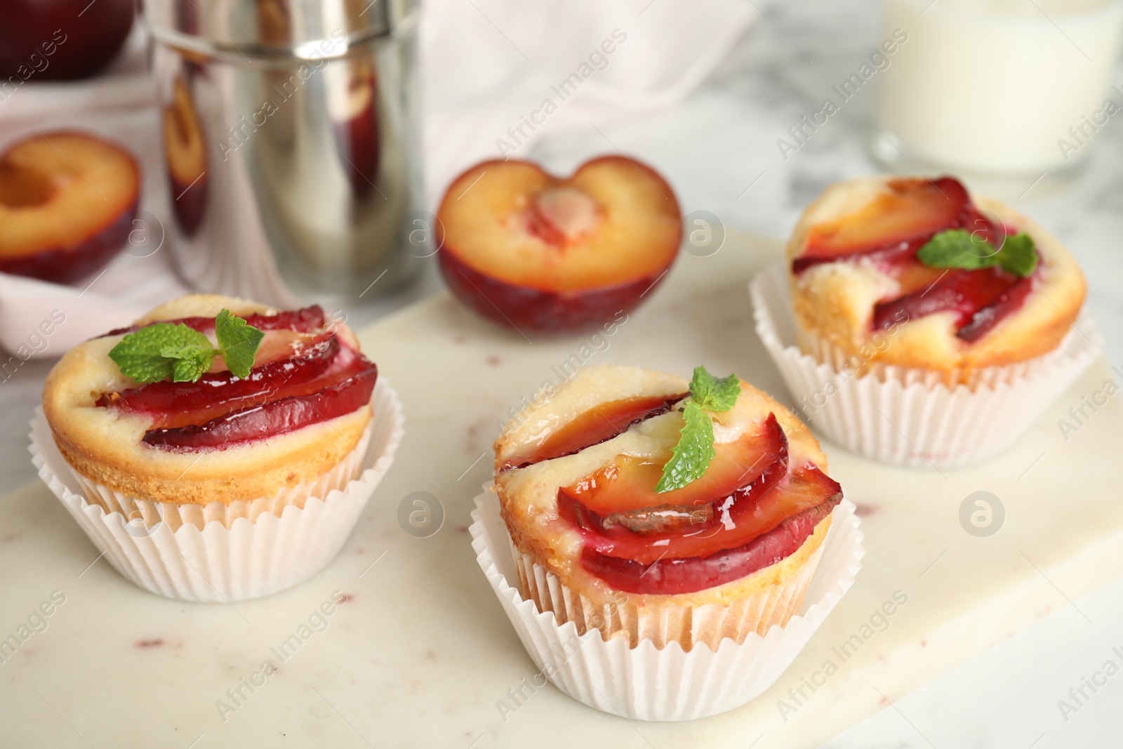 Photo of Delicious cupcakes with plums on white board, closeup