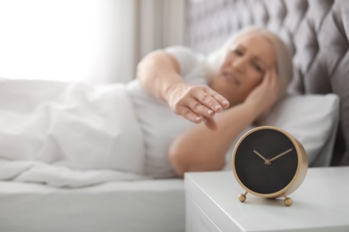 Mature woman with terrible headache trying to turn off alarm clock