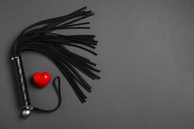 Photo of Black whip and red heart on dark background, flat lay with space for text. Sexual role play accessory