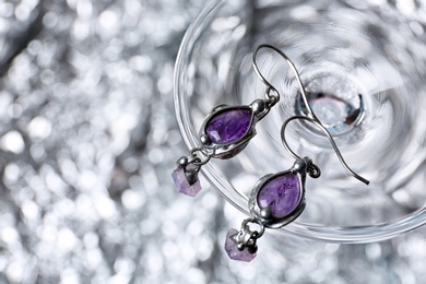 Photo of Beautiful pair of silver earrings with amethyst gemstones on blurred background, above view