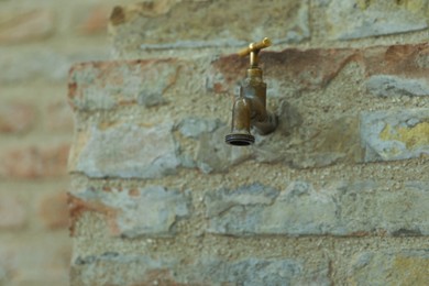 Metal water tap on old brick wall outdoors