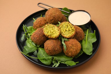 Photo of Delicious falafel balls, herbs and sauce on pale brown