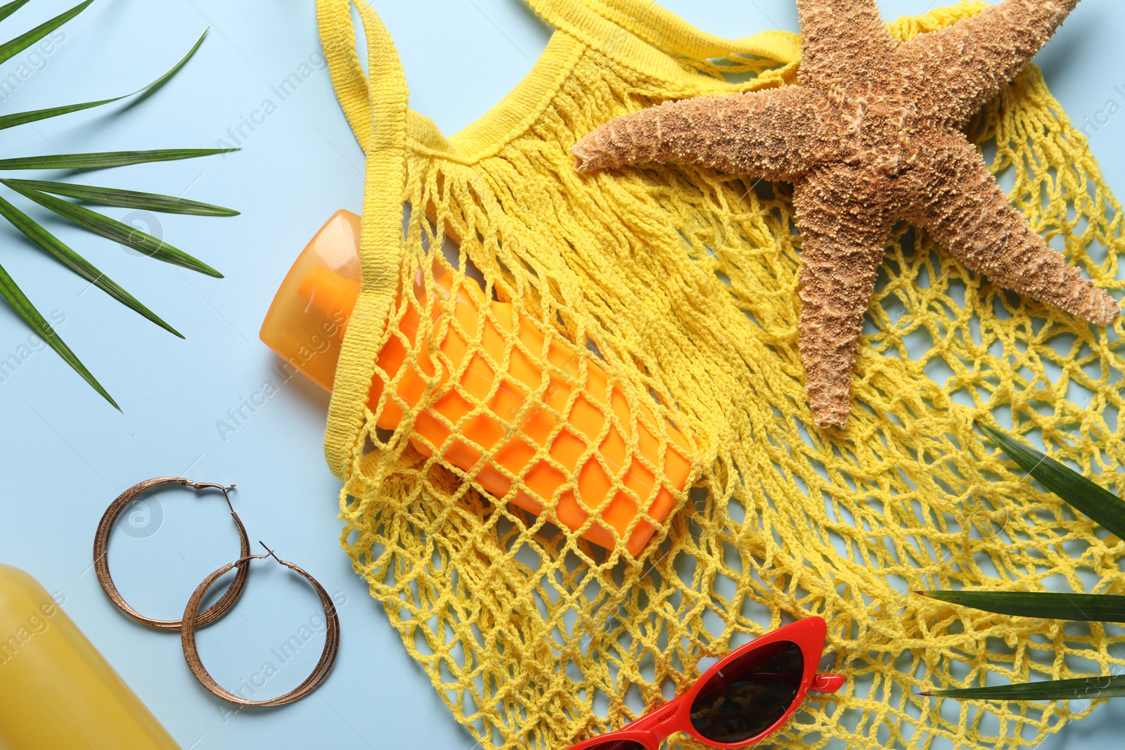 Photo of String bag, different beach accessories and palm leaves on light blue background, flat lay