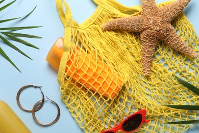 Photo of String bag, different beach accessories and palm leaves on light blue background, flat lay