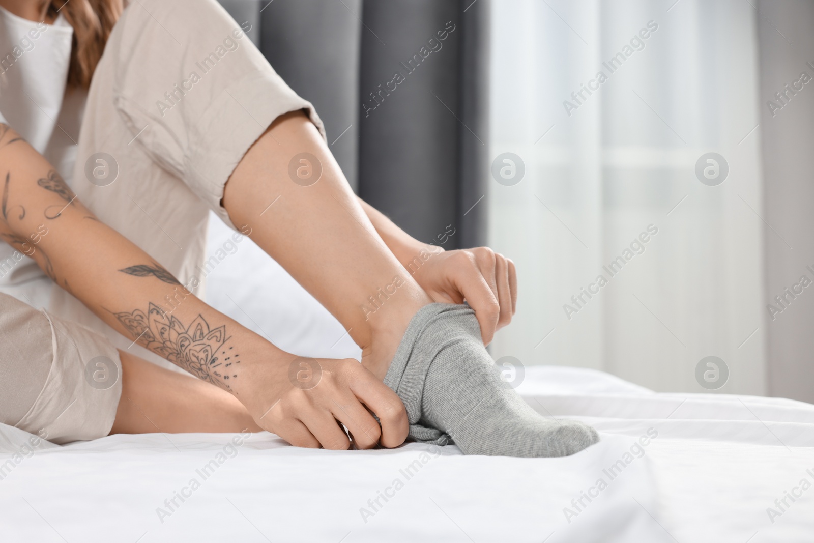 Photo of Woman putting on grey socks in bedroom, closeup
