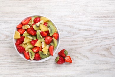 Photo of Delicious fresh fruit salad in bowl on white wooden table, top view. Space for text