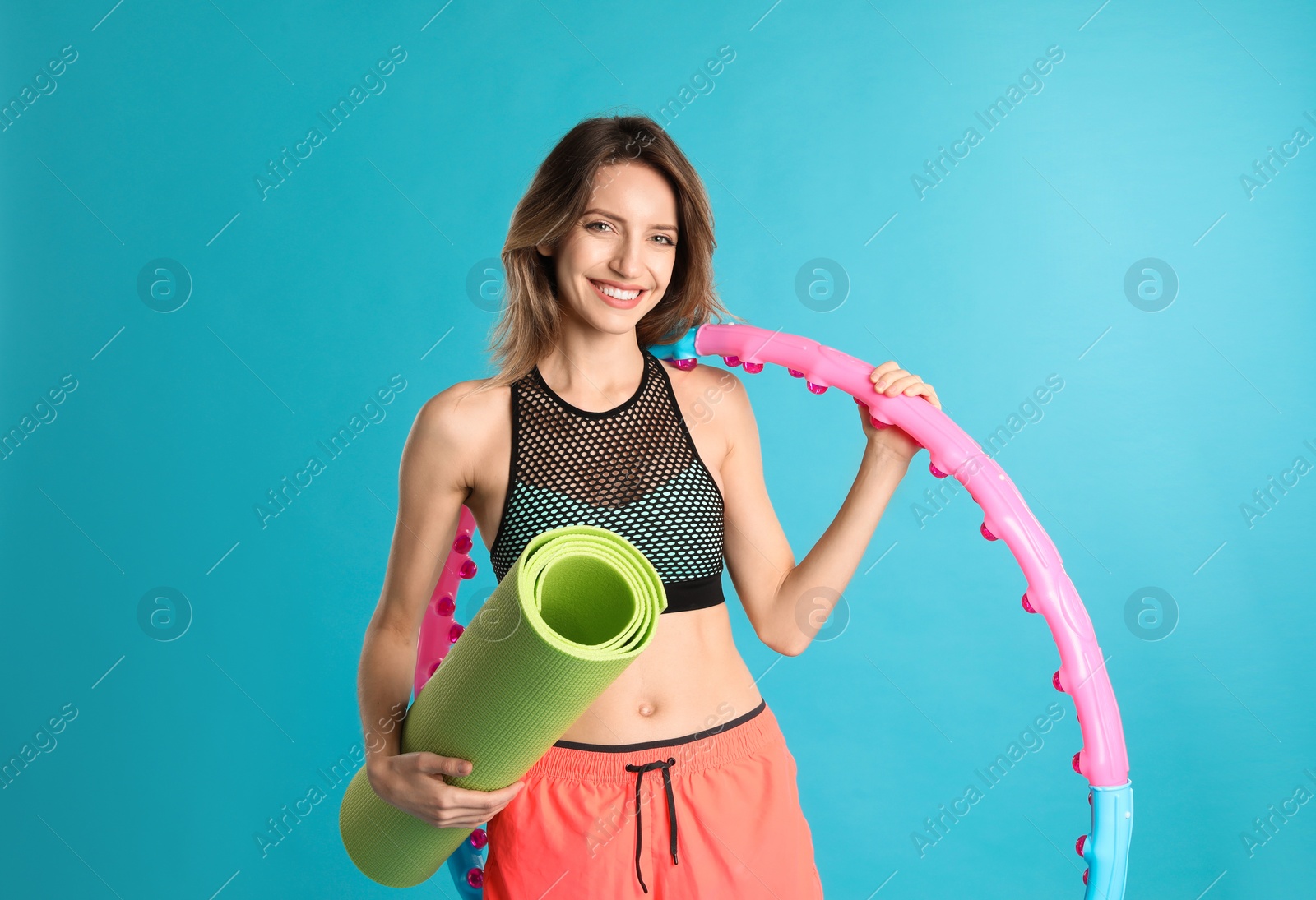 Photo of Beautiful woman with yoga mat and hula hoop on turquoise background